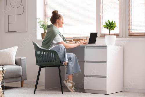 Young woman sitting at workplace and working with laptop in living room photo