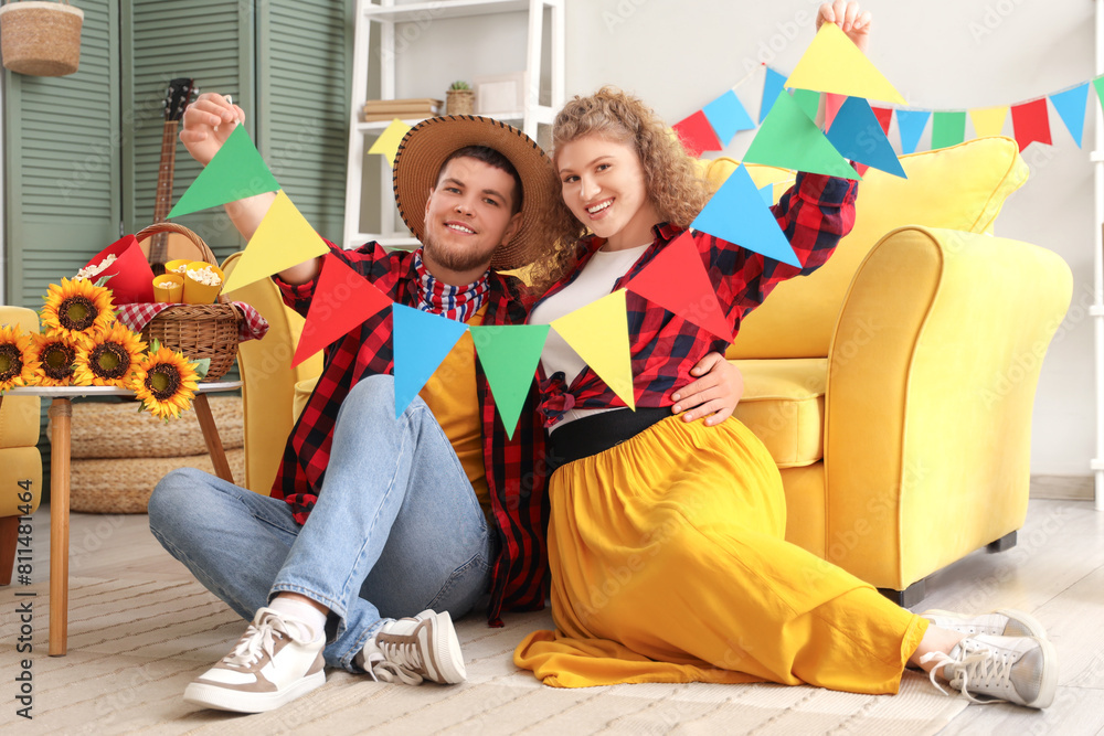 Obraz premium Happy young couple with colorful flags at home. Festa Junina celebration