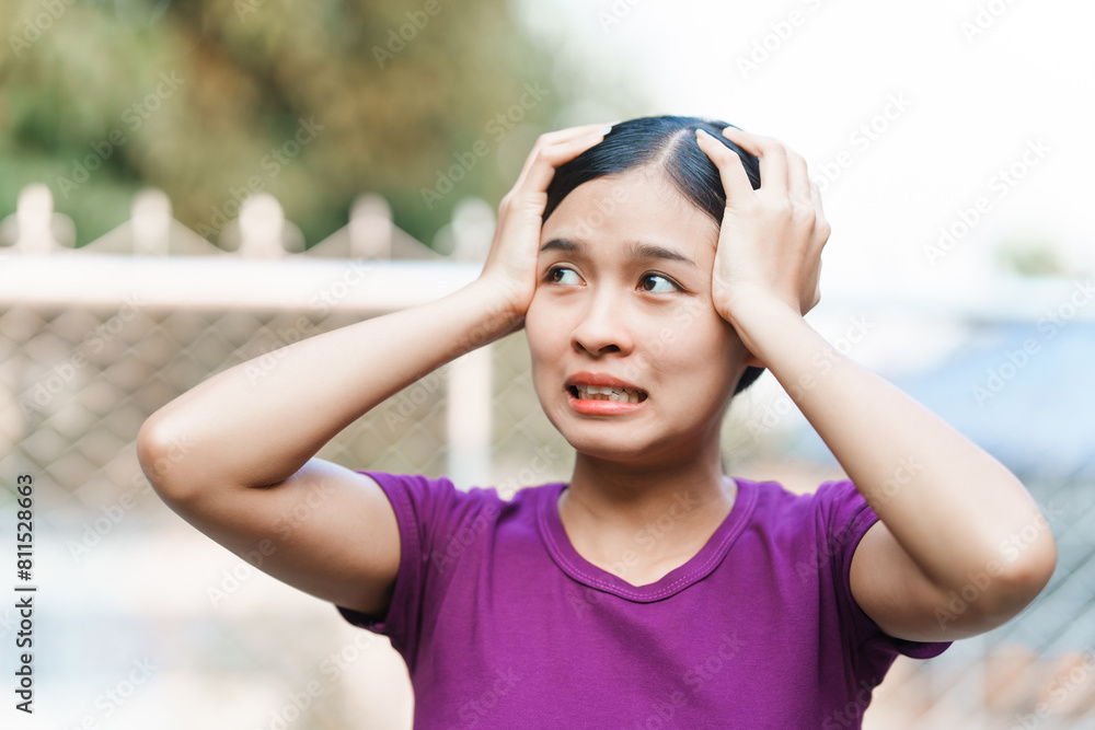 A young Asian woman appears panicked outside her home. She exhibits signs of anxiety, fear, and distress. Her expression reflects feelings of stress and unease.