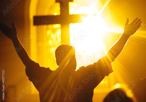 backlit image of a believer hands to heaven worshiping the cross photo