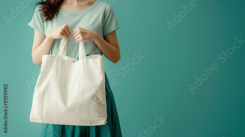 A person holding a blank white tote bag for branding mockup, against a teal background, suitable for a product presentation. Generative AI