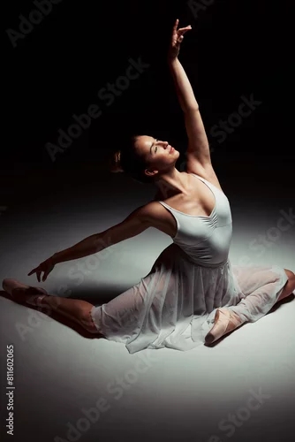 Obraz Sitting, ballerina and woman in studio for art performance, rehearsal or ballet routine. Spotlight, theater and female dancer for contemporary, dancing or elegant movement with dark background
