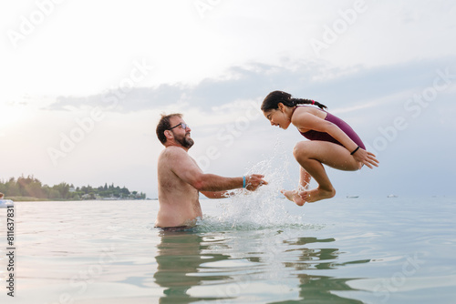 side view at girl full of splashes jumping in the water from the father arms