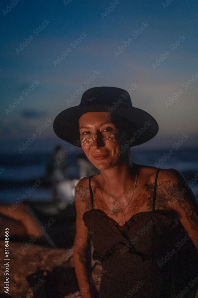 Portrait of a woman in a hat. Friends sitting by bonfire at beach. Portrait of a woman in a hat. Friends sitting by bonfire at beach.