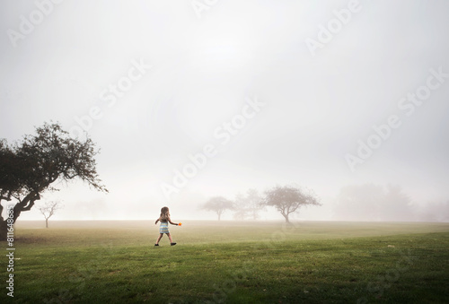 Young girl walking through foggy field holding bright orange leaf photo
