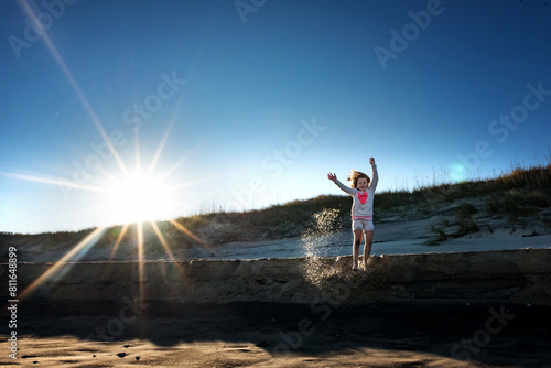 Happy tween girl jumping off sand dune with bright sunny beach photo