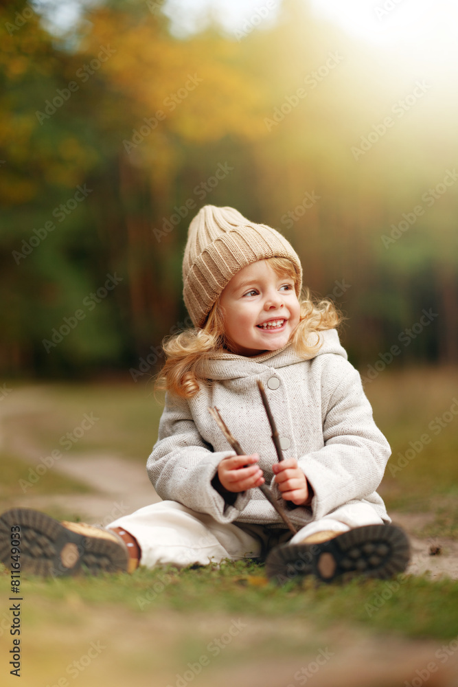 happy little girl sitting on the grass in the autumn forest at sunset happy little girl sitting on the grass in the autumn forest at sunset
