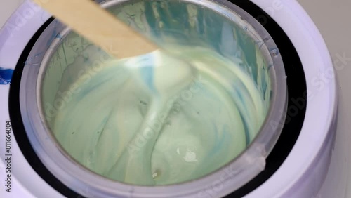 molten liquid film wax for depilation in a wax melt is stirred with a wooden spatula close-up, beauty background