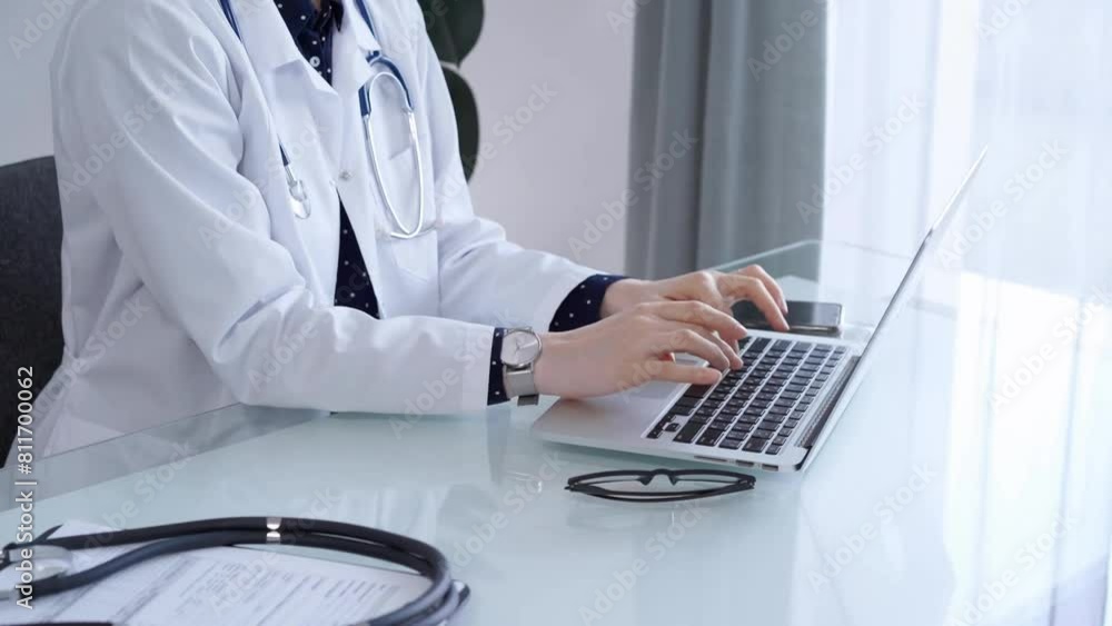Doctor woman is working with laptop computer at the glass table in clinic. Physician is typing medical information or giving advices online. Medicine and pharmacy Doctor woman is working with laptop computer at the glass table in clinic. Physician is typing medical information or giving advices online. Medicine and pharmacy
