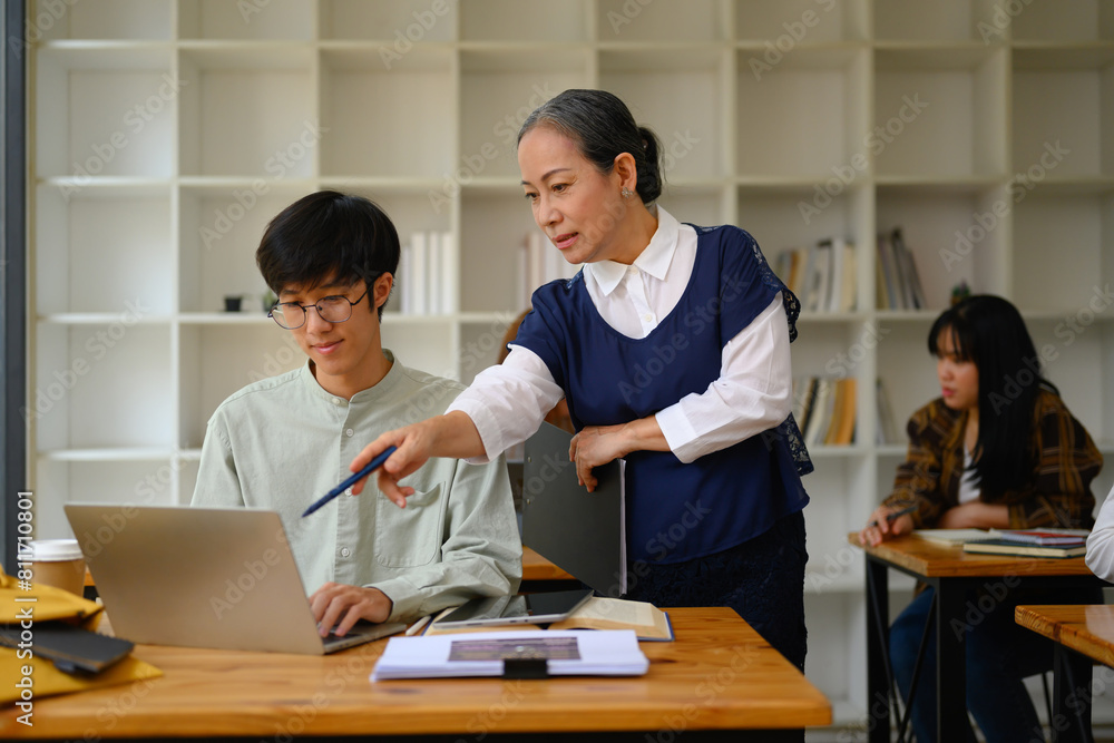 Shot of mature professor walking and checking student homework in the classroom Shot of mature professor walking and checking student homework in the classroom