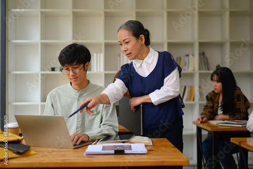 Shot of mature professor walking and checking student homework in the classroom photo