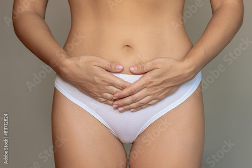 Cropped shot of a young woman in white panties holding her lower abdomen with hands suffering from painful periods on a dark background. Gynecological problems, genital tract infections, inflammation