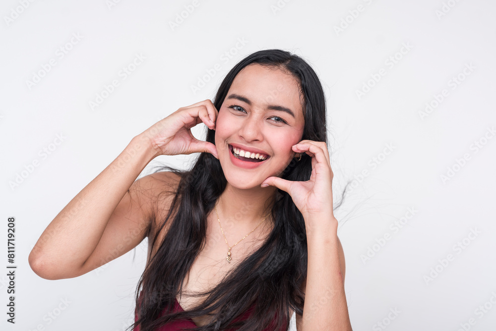 A portrait of a cheerful young Asian woman in a chic maroon dress, making a heart gesture with her hand between her cheeks, isolated on a white background. A portrait of a cheerful young Asian woman in a chic maroon dress, making a heart gesture with her hand between her cheeks, isolated on a white background.