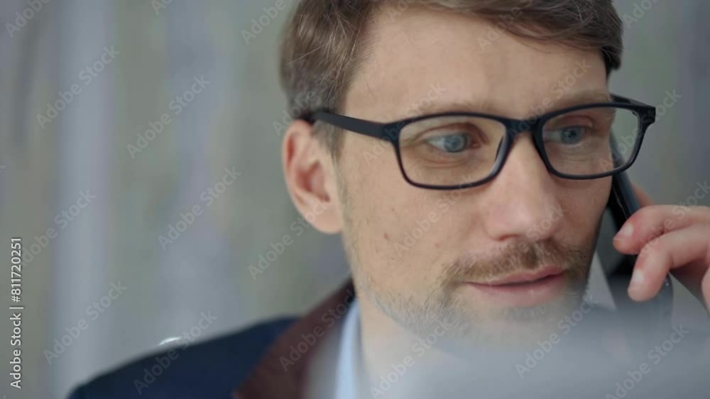 Businessman with glasses speaking on the phone, partially obscured by blurred laptop. Front view and close up portrait Businessman with glasses speaking on the phone, partially obscured by blurred laptop. Front view and close up portrait