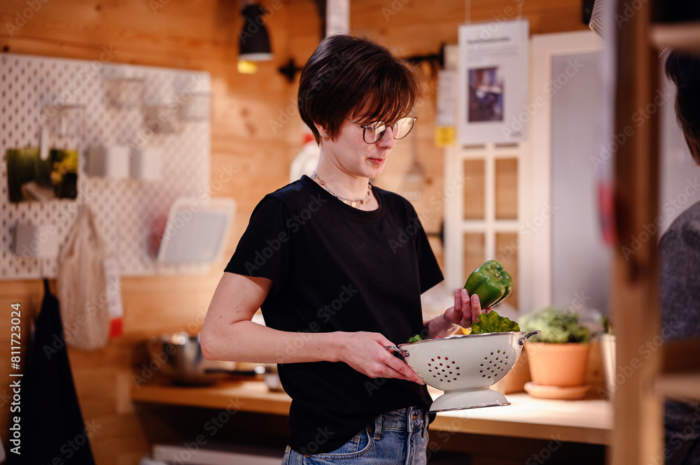 Fototapeta premium This image portrays a young adult focused on preparing fresh vegetables in a rustic kitchen. The scene is warmly lit