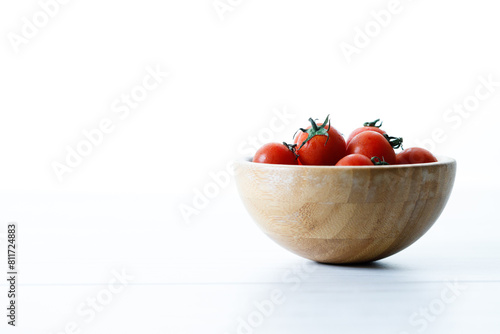 red cherry tomato in wooden bowl on white background