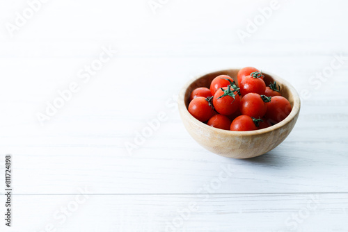 red cherry tomato in wooden bowl on white background