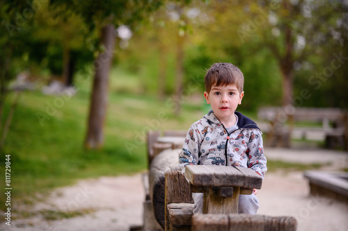 This image beautifully captures a pensive young boy sitting in a wooden structure at a park, surrounded by lush greenery. His contemplative gaze and the natural,  © Иванна Емельянова