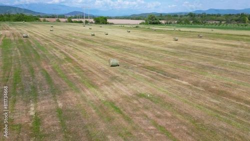 Aerial flyover shot of hay bales at a farm field in summer. Electricity trasmission wires over rural farmland on a warm spring day. Yellow hay and green grass. Drone footage of tod balesat a farm.
 photo