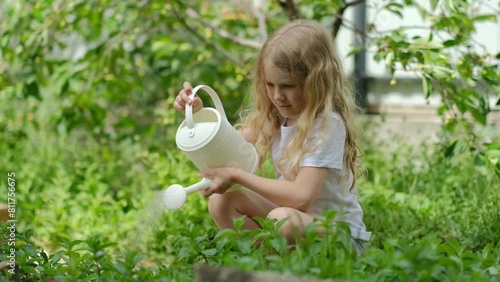 Caucasian happy curly child girl watering a plant in the backyard or country house. child gardener taking care of flowers. 4K