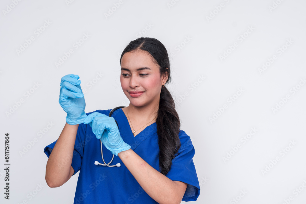 Young Asian female nursing aide in blue scrub suit, preparing for medical duties by putting on gloves, isolated on a white background. Young Asian female nursing aide in blue scrub suit, preparing for medical duties by putting on gloves, isolated on a white background.