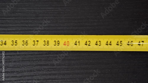 A yellow measuring tape is moving from right to left on a black background. photo