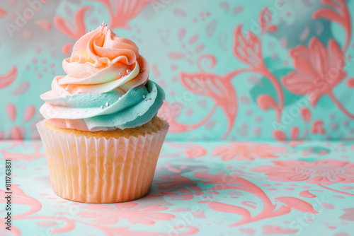 close up of a cupcake with peach and turquoise frosting on pastel floral background