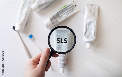 Dangerous toothpaste ingredient SLS, sodium laureth sulfate. Checking the composition of toothpaste with a magnifying glass against the background of many tubes photo