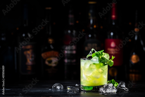 Green Negroni cocktail drink with gin, aperitif, liqueur, mint and ice. Black bar counter background with bottles © 5ph
