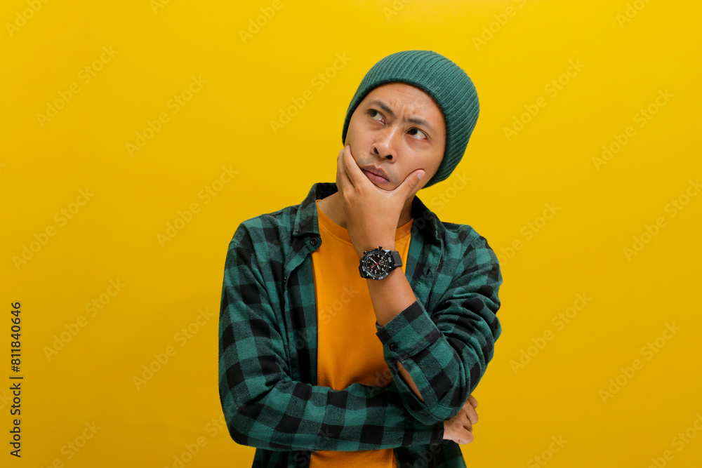 Thoughtful young Asian man, wearing a beanie hat and casual shirt, rests his hand on his chin, looking aside at empty copy space, deeply engrossed in thought and planning for the future Thoughtful young Asian man, wearing a beanie hat and casual shirt, rests his hand on his chin, looking aside at empty copy space, deeply engrossed in thought and planning for the future