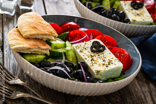 Greek style salad - fresh vegetables with feta cheese, pita bread and black olives served in bowl on wooden table 