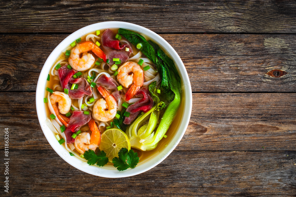 Shrimp and beef Pho soup - Vietnamese soup with shrimps and raw beef slices on wooden table
Shrimp and beef Pho soup - Vietnamese soup with shrimps and raw beef slices on wooden table