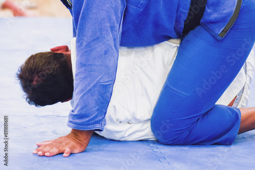 Two unidentifiable men practicing Brazilian Jiu-Jitsu on a blue mat