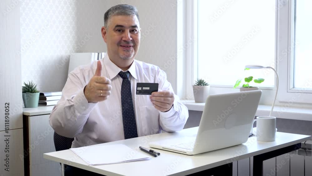 A man in a tie sits at a table, shows a bank card and gives a thumbs up. Suitable for advertising banking services, cards and terms of service. A man in a tie sits at a table, shows a bank card and gives a thumbs up. Suitable for advertising banking services, cards and terms of service.