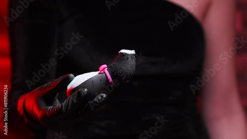 Vibrator in the shape of a penguin. A vacuum-wave clitoral stimulator in the hand of a girl in black latex gloves and a black dress on a red background. Droplets of water splash from the toy
