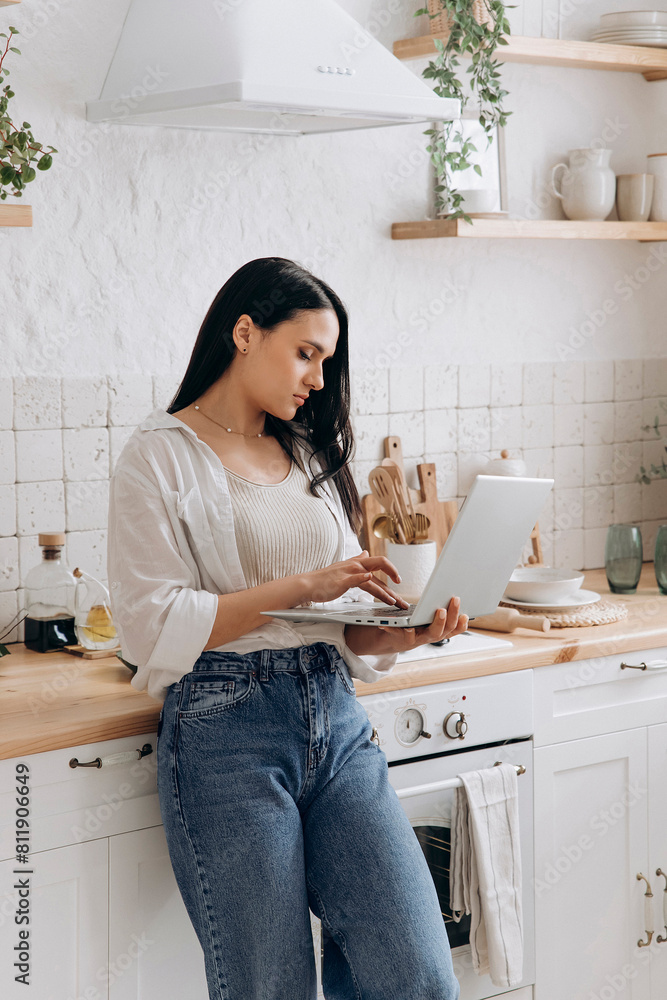 Young woman freelancer or student working on a laptop in her kitchen, taking breaks between household chores or cooking. Perfect for content about balancing education, work, and home life Young woman freelancer or student working on a laptop in her kitchen, taking breaks between household chores or cooking. Perfect for content about balancing education, work, and home life