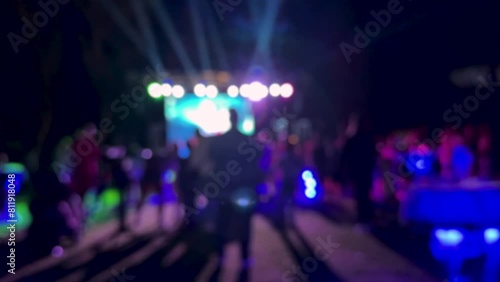 Crowd of people dancing on the dance floor of a night club under the light of colored spotlights and laser. People jump and raise their hands up