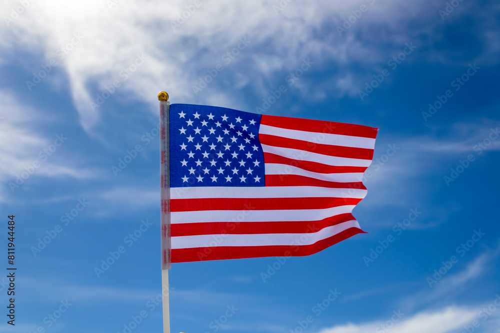 Obraz premium American flag fluttering in the wind against blue sky and white clouds