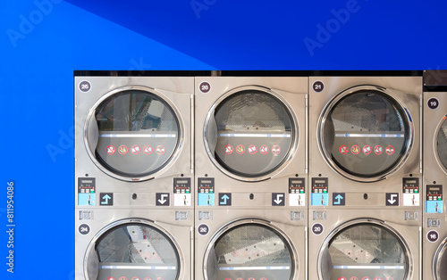 Rows of vending washing machines and clothes dryers on blue smartboard wall background in modern laundromat shop