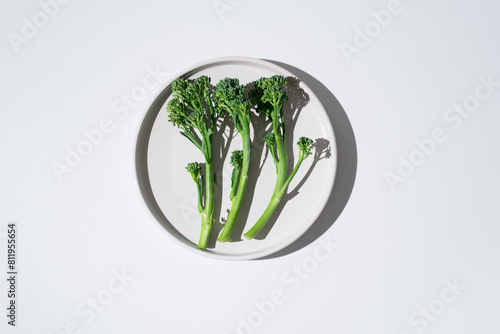 Brócoli broccolini bebé crudo dentro de un plato sobre fondo blanco. Vista superior photo
