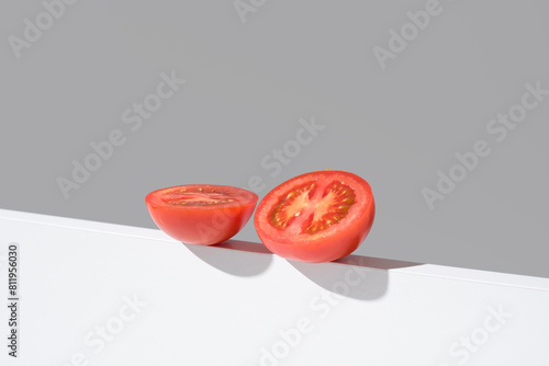 Un tomate maduro cortado por la mitad sobre un soporte blanco y fondo gris	