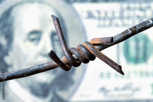 Economic confrontation and warfare, sanctions and embargo busting concept. Barbed wire against US Dollar bill. Macro image.