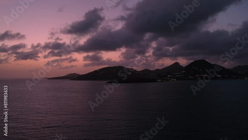 Outline of Sint Maarten in background of pink sunset sky and dusk clouds, view from cruise ship sailing in Great bay on lights of evening Philipsburg
