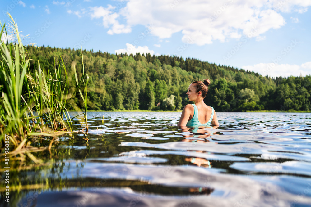 Swimming in lake in Finland. Woman in summer at beach. Finnish bathing in water in nature. Back view of person. Blue sky and beautiful green forest. Relax in Scandinavia after cottage sauna. Swimming in lake in Finland. Woman in summer at beach. Finnish bathing in water in nature. Back view of person. Blue sky and beautiful green forest. Relax in Scandinavia after cottage sauna.