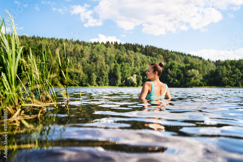 Swimming in lake in Finland. Woman in summer at beach. Finnish bathing in water in nature. Back view of person. Blue sky and beautiful green forest. Relax in Scandinavia after cottage sauna.