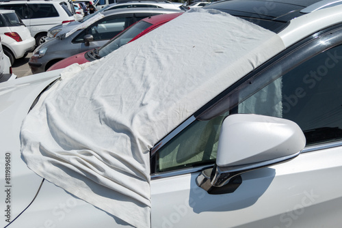white car windshield is covered with white bedsheet to prevent heating on a parking lot at hot sunny summer day in Asia, closeup