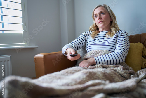 Mature Economically Inactive Woman Suffering With Long Term Illness On Sofa At Home Watching TV
