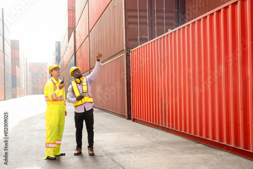 Two diverse container workers working at dock site,foreman control loading containers box from cargo freight ship holding walkie talkie,african male using digital tablet inspect cargo container boxes