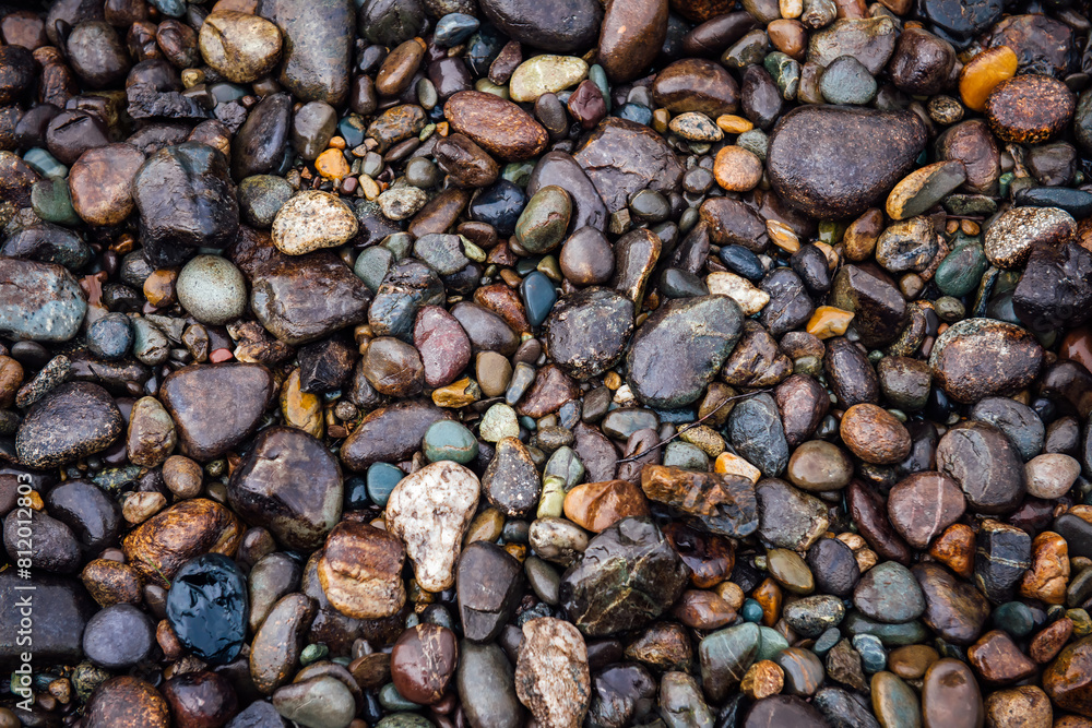 Abstract river colorful pebble stones background. Pattern of wet rocks gracefully arranged. Each stone glistens in the gentle water, creating an intricate mosaic of earthy colors and textures Abstract river colorful pebble stones background. Pattern of wet rocks gracefully arranged. Each stone glistens in the gentle water, creating an intricate mosaic of earthy colors and textures