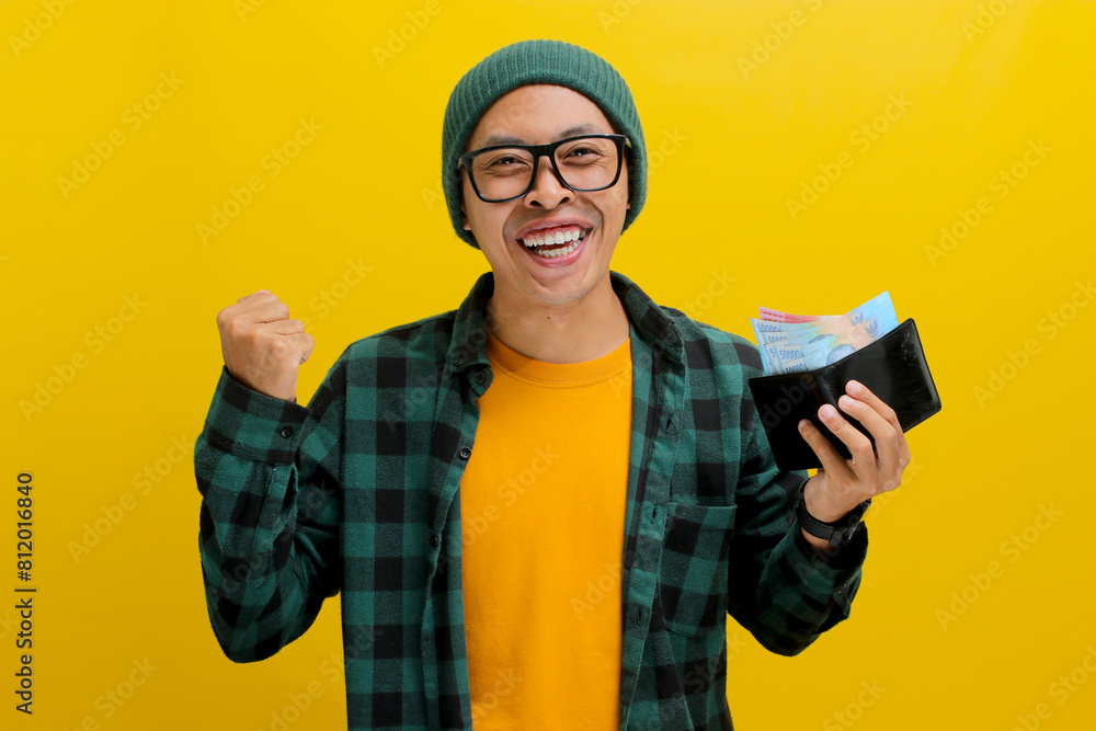 Excited Asian man, dressed in a beanie hat and casual shirt, smiles at the camera while proudly displaying a wallet filled with money, representing finance, investment, and money saving concepts Excited Asian man, dressed in a beanie hat and casual shirt, smiles at the camera while proudly displaying a wallet filled with money, representing finance, investment, and money saving concepts